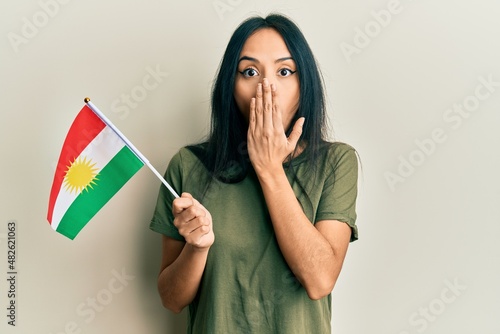 Foto Young hispanic girl holding kurdistan flag covering mouth with hand, shocked and afraid for mistake