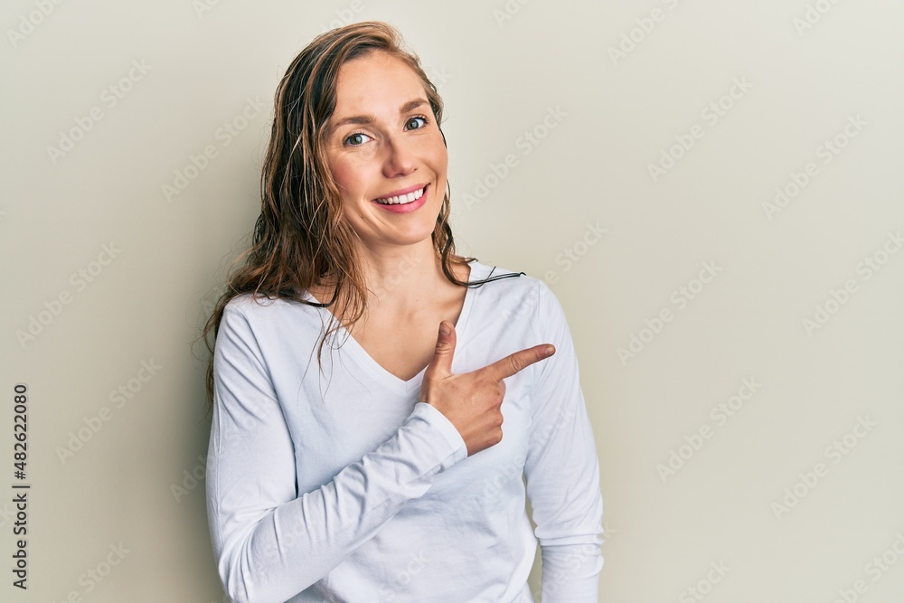 Young blonde woman wearing casual clothes cheerful with a smile of face pointing with hand and finger up to the side with happy and natural expression on face Young blonde woman wearing casual clothes cheerful with a smile of face pointing with hand and finger up to the side with happy and natural expression on face
