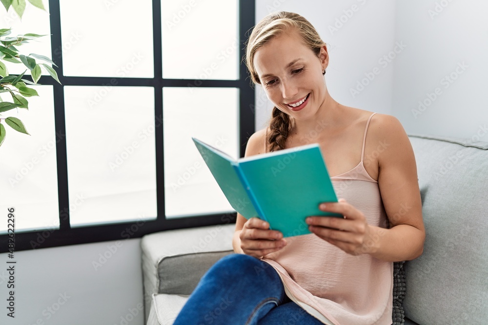 Young caucasian woman reading book sitting on sofa at home Young caucasian woman reading book sitting on sofa at home