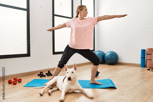 Young caucasian woman training yoga with dog at sport center