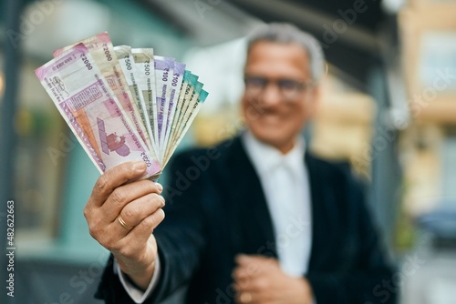 Middle age southeast asian man holding indian rupees banknotes at the city