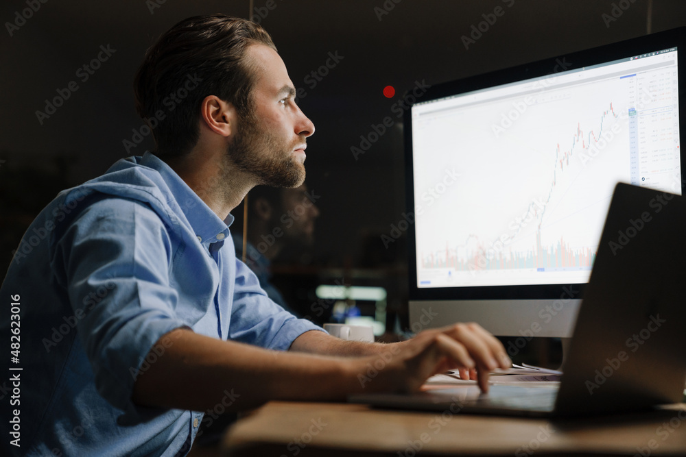 Young man working with laptop and computer while sitting at desk Young man working with laptop and computer while sitting at desk
