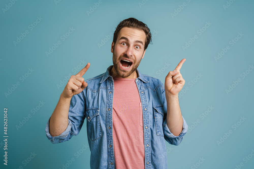Young bristle man pointing finger aside while expressing surprise Young bristle man pointing finger aside while expressing surprise