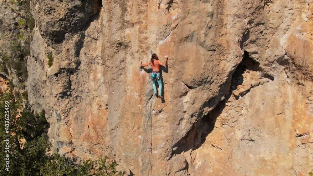 aerial drone view of strong muscular man rock climber with long hair climbing on high rocky wall, crag by challenging rock climbing route. Rock climbing outdoors aerial drone view of strong muscular man rock climber with long hair climbing on high rocky wall, crag by challenging rock climbing route. Rock climbing outdoors