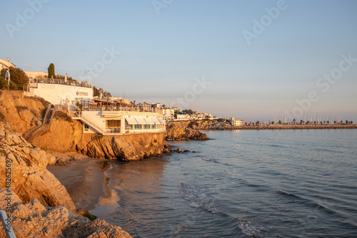 Barcelona, Spain - November 20, 2021: Rest at the sea. Evening landscape with architecture, cafe on the background of the azure sea. Evening in the city of Sitges, Spain, Catalonia.