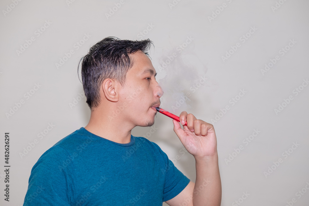 An asian man smoking an e-cigarette or vaporizer. An asian man smoking an e-cigarette or vaporizer.