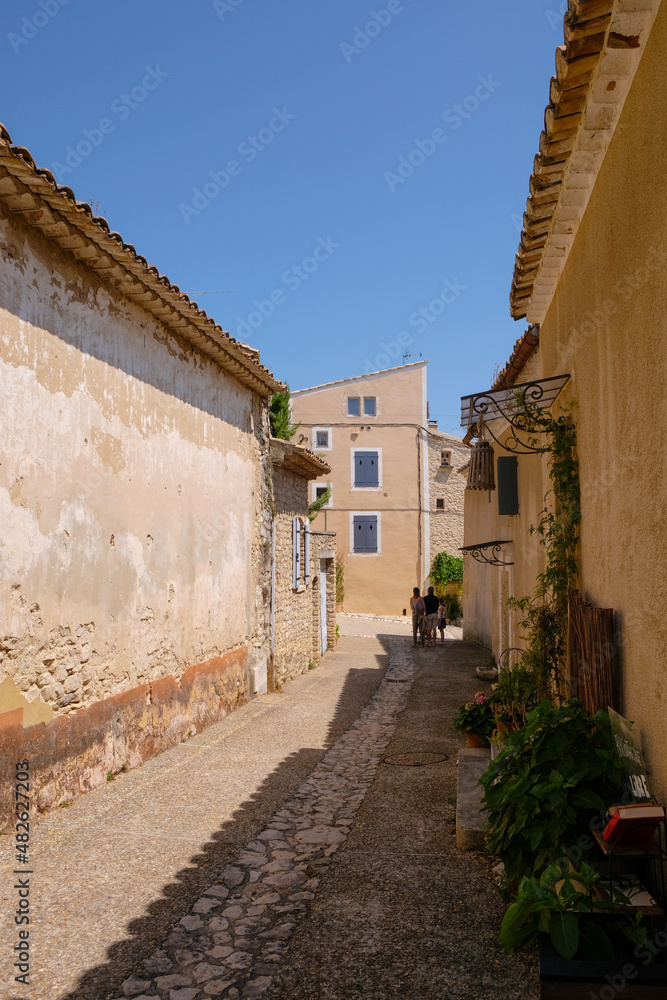 Joucas, Provence, France. August 08, 2021. Old stone street with tourist family and street's library. Local tourism. Vertical image. 
