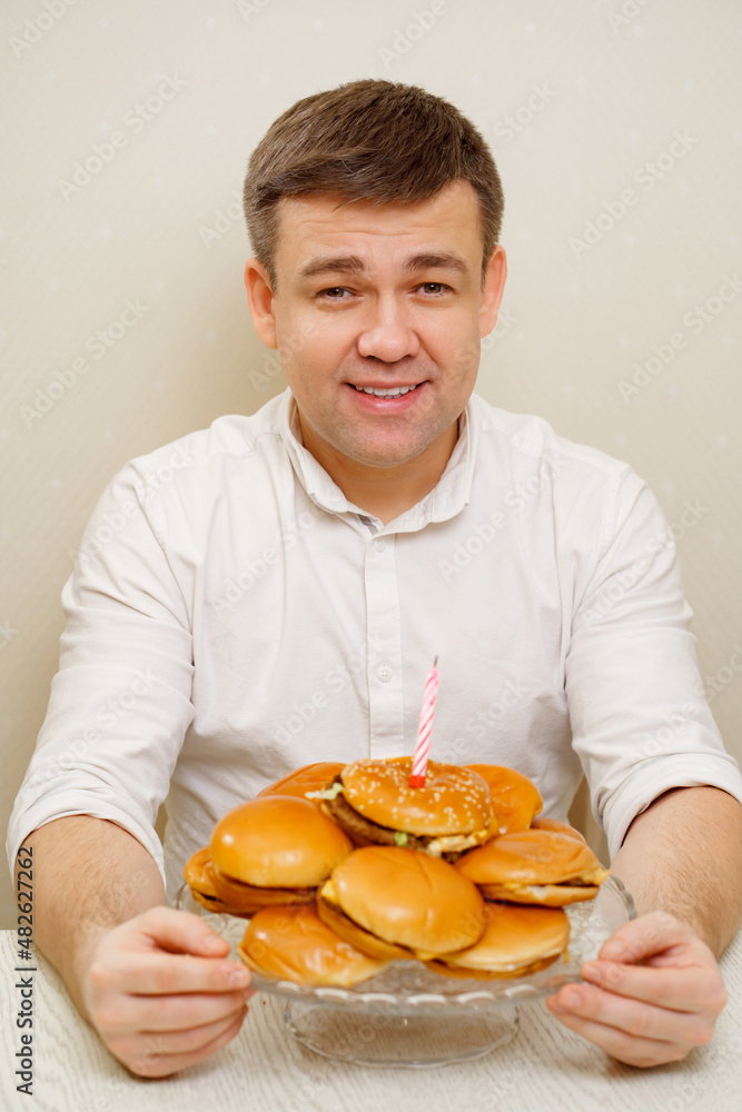 happy man makes wish and blows out candle on hamburger cake. cake for men. happy man makes wish and blows out candle on hamburger cake. cake for men.