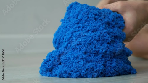 Close-up view of woman's hands with kinetic sand of bright blue color. She plays with kinetic sand stirring it in her hands. Anti-stress toy for children and adults. Sand is pouring from hands. photo