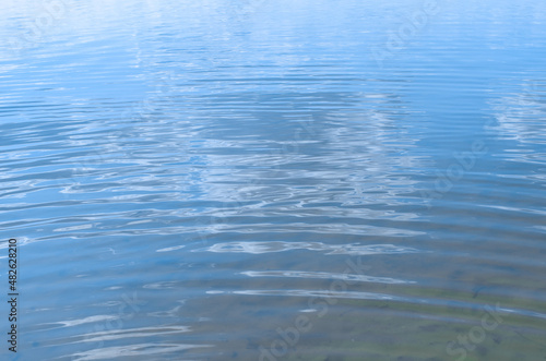 Clear blue sea or lake outdoors, close-up. Texture of water ripples on sunny summer day, perspective view, selective focus
