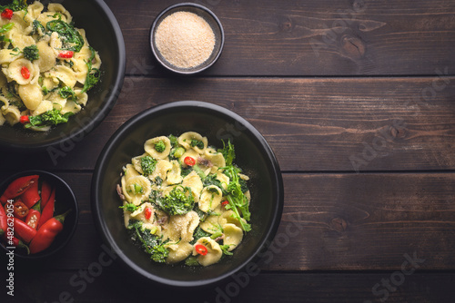 Italian pasta Orecchiette with turnip leaves (cima di rapa) and tops with garlic, hot pepper, grated bread on a dark wooden background. Recipes of southern Italy, Puglia. Poor cuisine, close up
