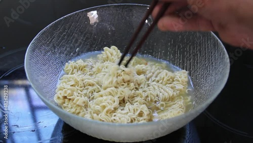 Using chopsticks, stir instant noodles soup in a bowl with hot water.