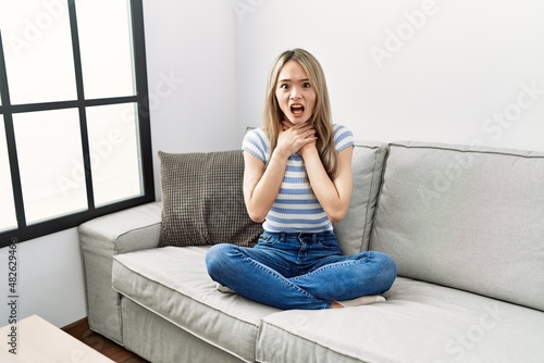 Asian young woman sitting on the sofa at home shouting and suffocate because painful strangle. health problem. asphyxiate and suicide concept.