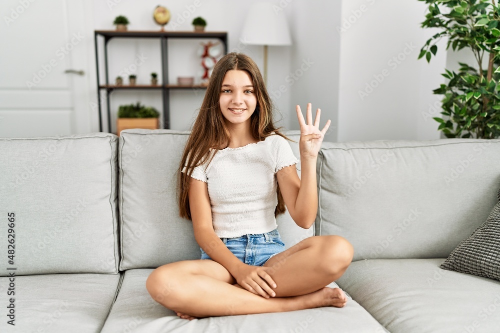 Young brunette teenager sitting on the sofa at home showing and pointing up with fingers number four while smiling confident and happy. Young brunette teenager sitting on the sofa at home showing and pointing up with fingers number four while smiling confident and happy.