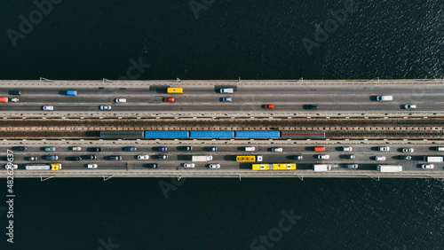 Aerial top view of cars and subway passing the bridge over the river in the city