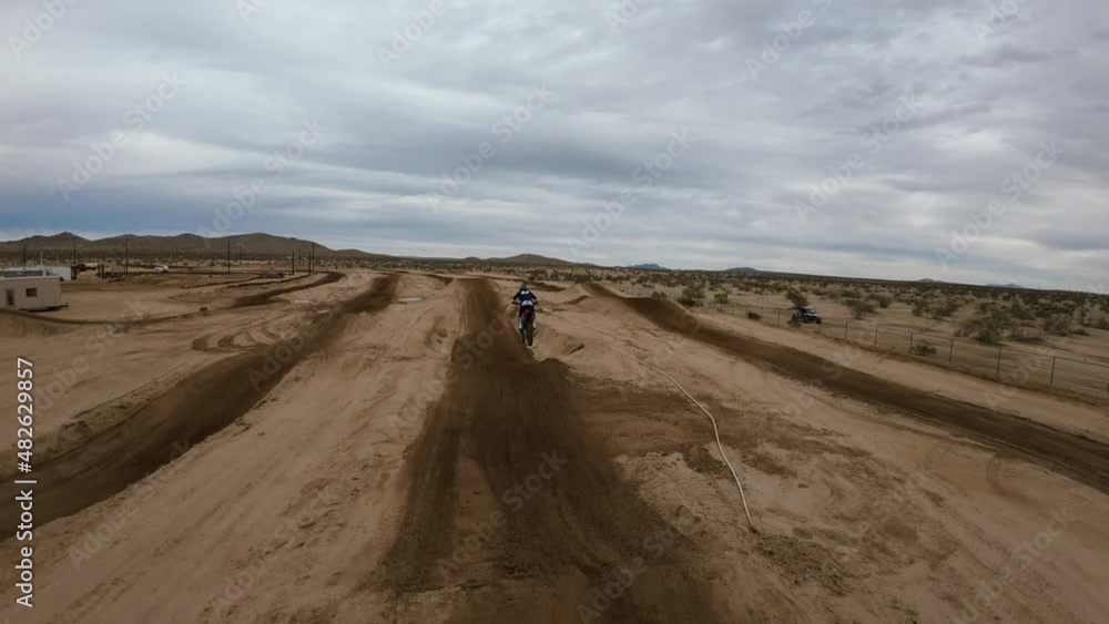 First-person drone following a motorcycle over a jump on a racetrack in the Mojave Desert in slow motion First-person drone following a motorcycle over a jump on a racetrack in the Mojave Desert in slow motion