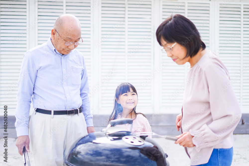 Obraz premium 孫とバーベキューをする高齢の夫婦