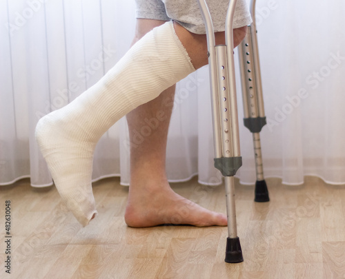 Close-up of man leg in plaster cast using crutches while walking.