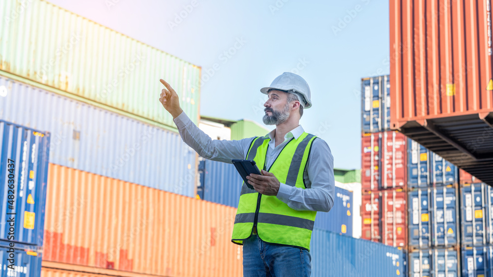 CEO or Manager in white helmet with tablet control loading Containers box in warehouse , manager inspector or Safety Supervisor in Container CustomTerminal port concept import export transportation 