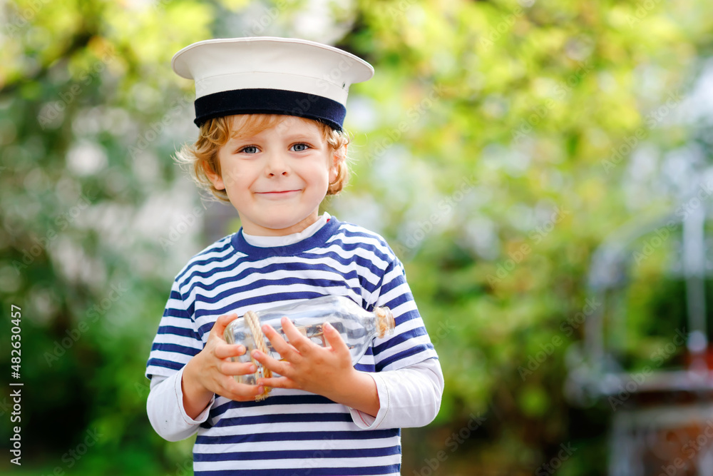 Happy little kid boy in sailor capitain hat and uniform playing with sailor boat ship. Smiling preschool child dreaming and having fun. Education, profession, dream concept