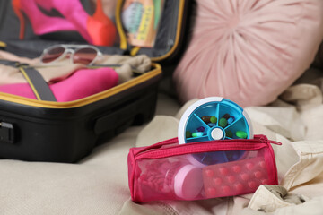 Pouch with different medicaments and pill box near packed suitcase on sofa