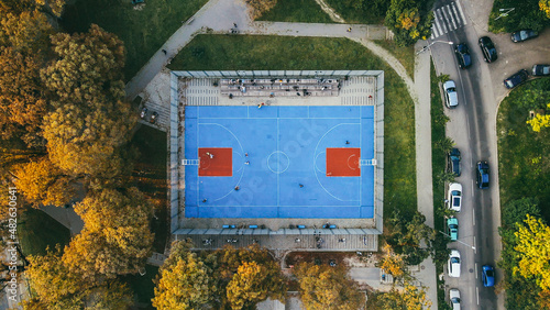 Top view of the blue stadium in the park, teenagers playing basketball in autumn