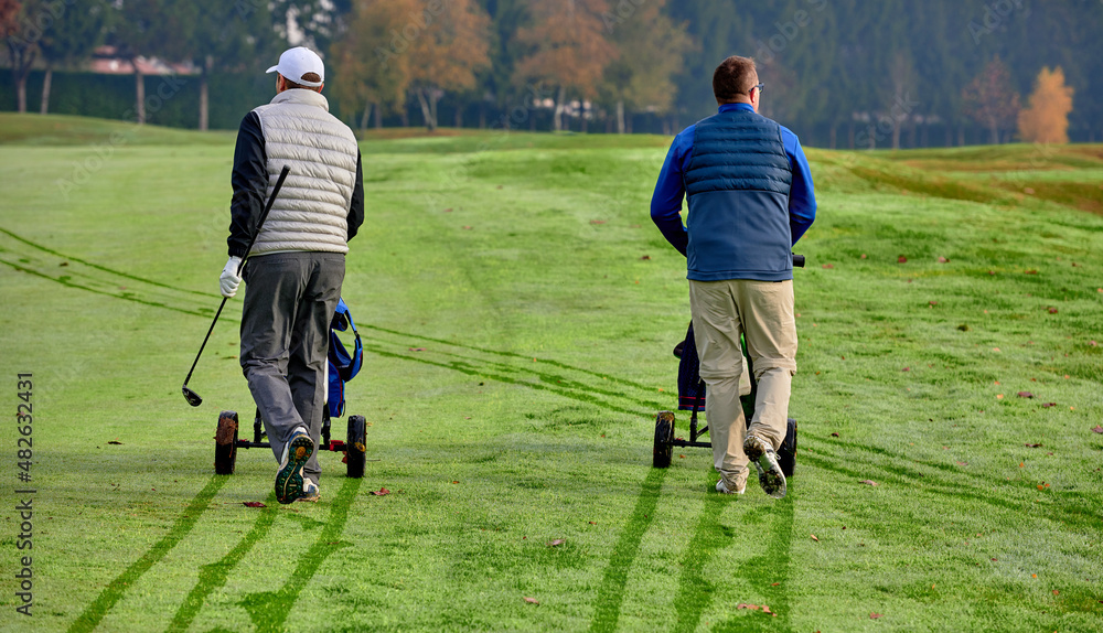 Obraz premium Golfers on a golf course in winter with frost covering the grass, pushing the cart up to the ball.
