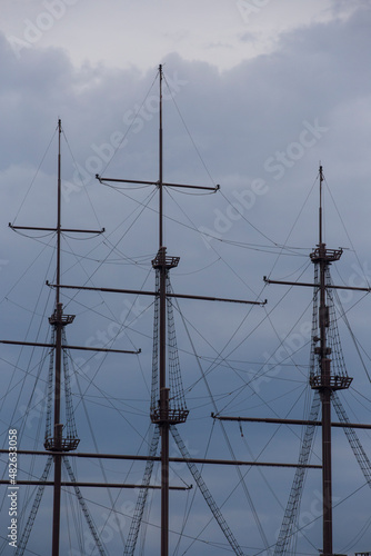 three wooden masts of a Dutch fluyt merchant sailing ship of XVIII century on a grey sky and clouds background close up vertical view photo