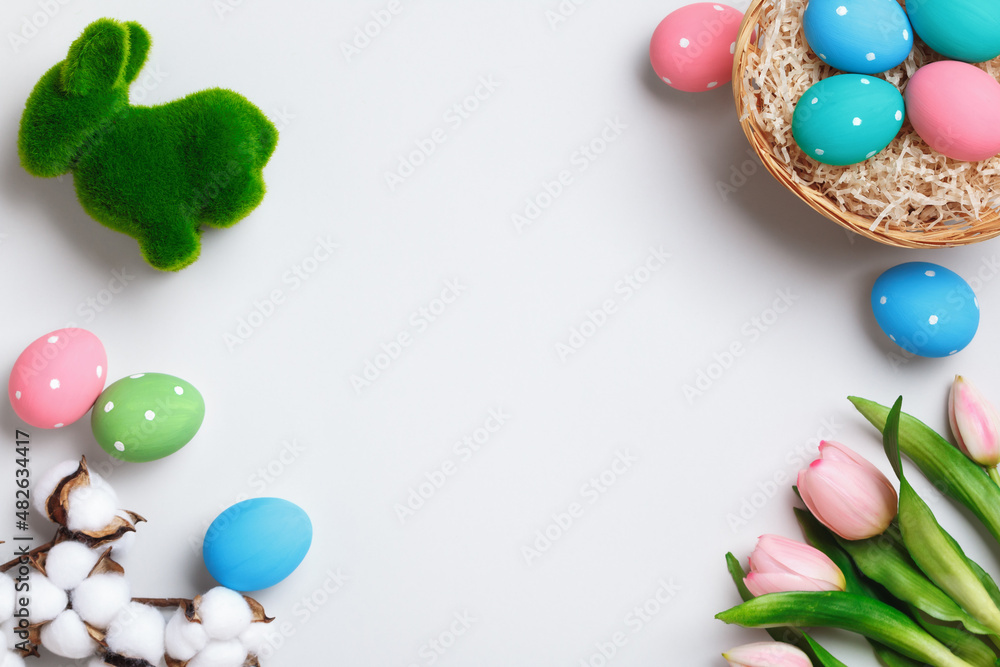 Easter composition. Multi-colored eggs in a basket, tulips rabbit flowers on a gray background. Flat lay top view copy space for greeting cards.