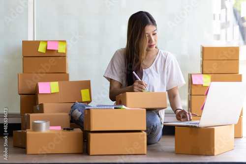 A young woman running a small online business is writing a shipping address on a parcel. © Wasan