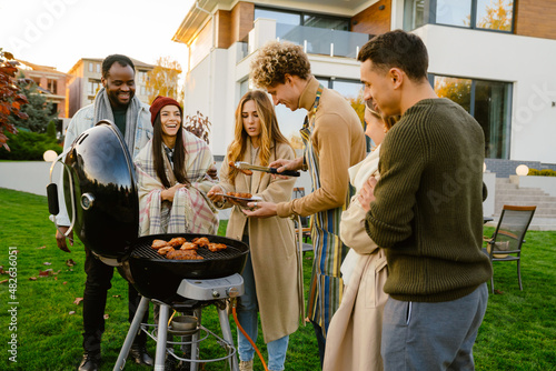 White man grilling meat during barbeque with his friends on backyard photo