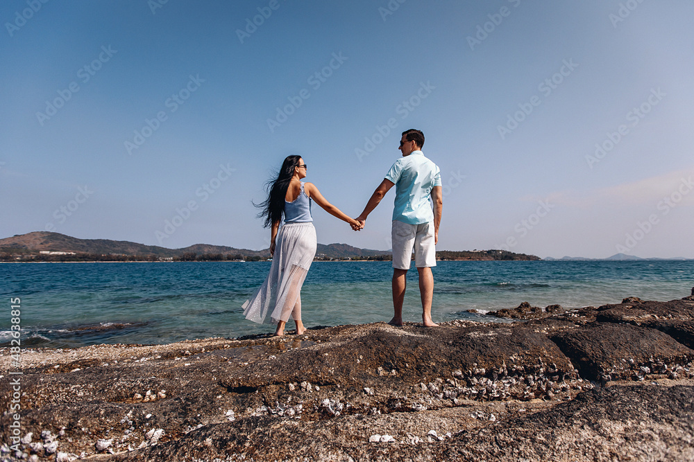 Young and beautiful lovely couple walking on the beach against the background of the sea and clear sky. Concept of tohetherness. Young and beautiful lovely couple walking on the beach against the background of the sea and clear sky. Concept of tohetherness.