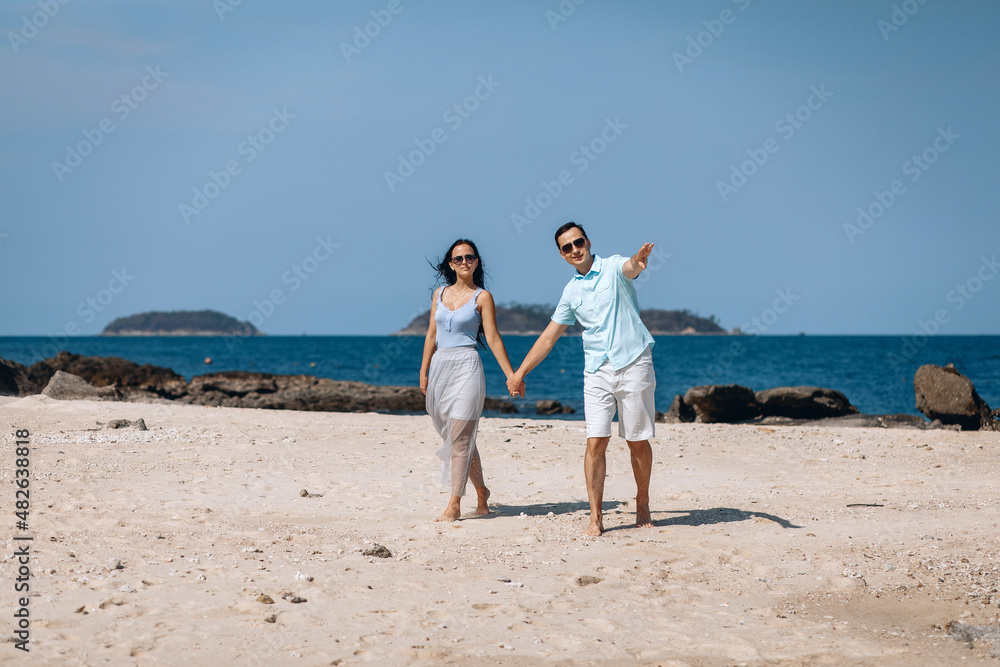 Beautiful attractive woman standing on the beach looking where the handsome man pointing and holding her hand. Concept of relationship. Beautiful attractive woman standing on the beach looking where the handsome man pointing and holding her hand. Concept of relationship.