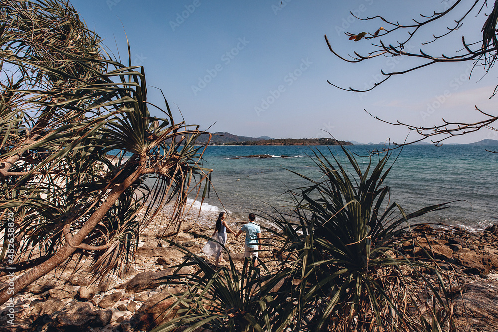 Confedent young man and his beautiful pretty woman standing under a palm tree against the sea and looking into the distance. Romance concept.