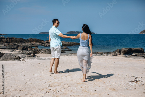 Young successful man and beautiful lovely woman in blue clothes standing under a palm tree against the sea and looking into the distance. Concept of love.