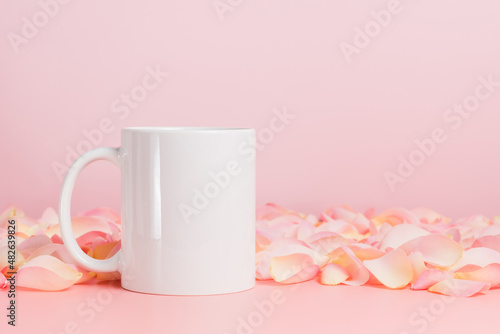Mockup white mug or coffee cup on pink background with rose petals. Blank template mug for advertising, text or design