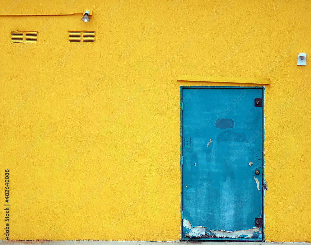 Bright blue, urban, industrial metal door is on a bright , yellow stucco building Bright blue, urban, industrial metal door is on a bright , yellow stucco building