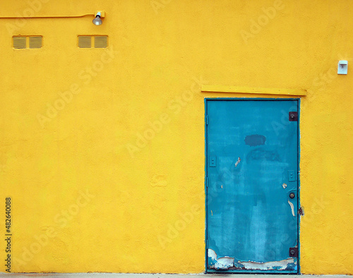 Bright blue, urban,  industrial metal door is on a bright , yellow stucco building © Robin Keefe
