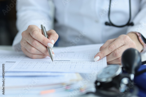 Doctor cardiologist examining patient cardiogram on paper in clinic closeup