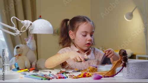 Preschool-age girl wants to become a fashion designer when she grows up. Child creates clothes for his dolls sitting at home at the table. child is playing with dolls in the bedroom at the table