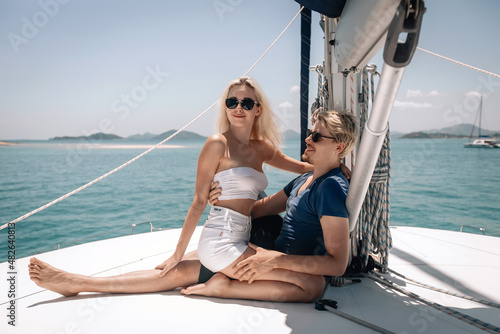 Portrait of a lovely beautiful couple posing on their expensive white yacht. Sexual woman sitting on the lap of a guy, and a handsome guy hugging her waist with a smile. Summertime concept