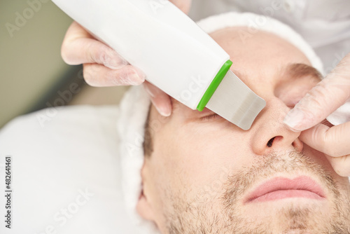 Ultrasound cosmetology scrubber. Face cavitation procedure. Salon skincare treatment. Professional peeling hardware. Electric spa equipment. Medicine patient device. Removal acne photo