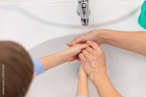 Mom helps the child wash his hands under running water from the faucet in the sink at home in the bathroom. Selective focus. Close-up