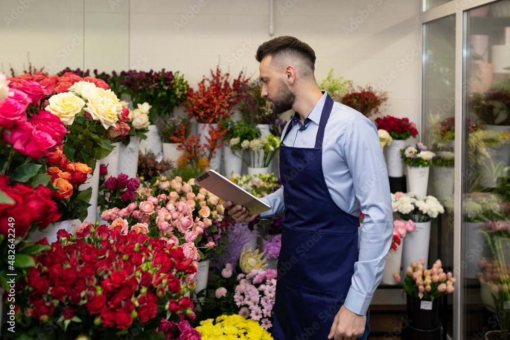 young male florist inside a flower refrigerator examines bouquets