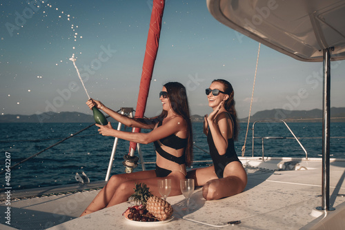 Portrait of two adult nice and happy lesbians celebrating an event on their yacht and having fun surrounded by fruits and champagne against a background of water and a clear sky. Summertime concept © Semachkovsky 