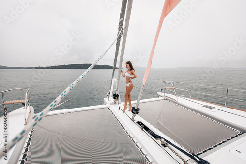 Amazing fit sexy woman in a tight white bikini is standing between two yacht polyester nets, wide angle © Semachkovsky 