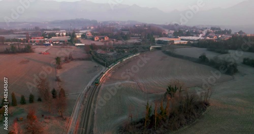 Train passing through countryside early morning, aerial shot following the subject.