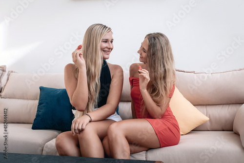 Two young beautiful blond ladies are looking at each other and smiling, eating strawberries