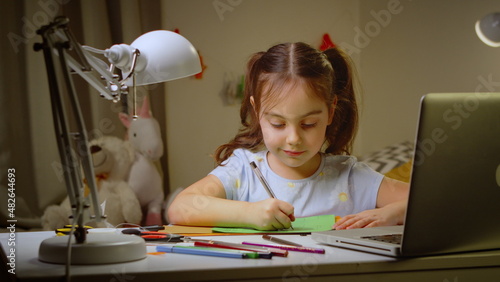 Smart cute preschool girl enjoying creativity by drawing a coloring with pencils while sitting at the table in the bedroom. the concept of children's development.