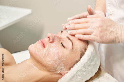 Face massage prepare at spa salon. Doctor hands. Pretty female patient. Beauty treatment. Healthy skin procedure. Young woman head. Cleaning rejuvenation. Facial dermatology mask. Detox therapy